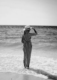 Rear view of woman standing in shallow water at seashore against sky