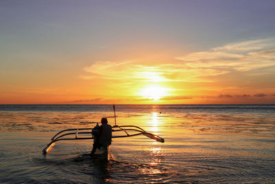 Rear view of silhouette man sitting on boat in sea against sky during sunset