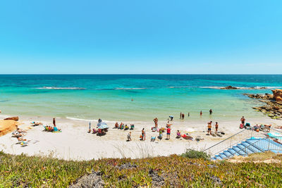 People at beach against clear blue sky