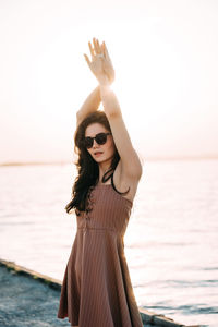 Young woman wearing sunglasses standing at beach against sky