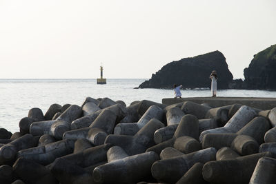 Friends on jetty by tetra pods at beach against clear sky