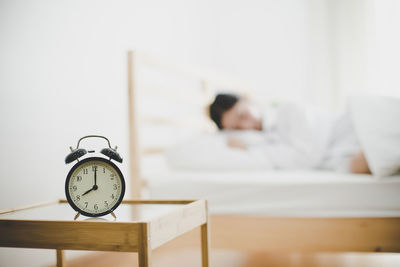 Close-up of alarm clock on side table against woman sleeping at home 