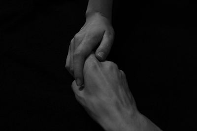 Cropped image of people holding hands against black background