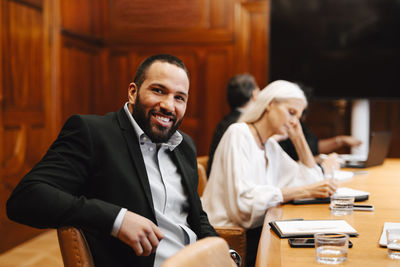 Portrait of smiling businessman sitting at conference table in board room during meeting