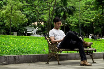 Young woman sitting on seat against trees