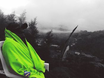 Side view of man sitting by tree in forest against sky