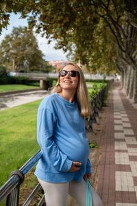 Pregnant woman looks at the sun in sunglasses. mom-to-be in a hoodie walks around the city