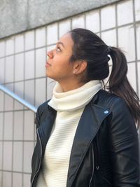 Side view of young woman looking away against wall