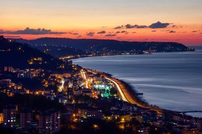 High angle view of illuminated city by buildings against sky during sunset