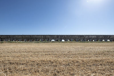 Arch bridge on field against clear blue sky