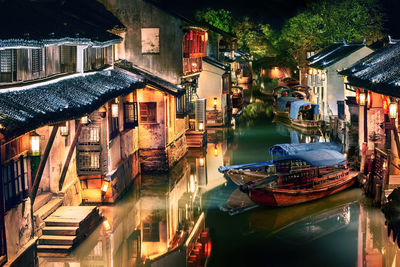 Boats moored in canal amidst buildings in city at night