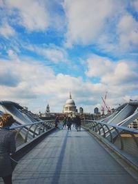 People walking on millennium bridge against cloudy sky