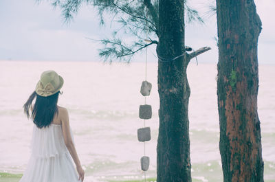 Rear view of woman standing by decoration hanging from tree against sea