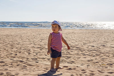 Child in a t-shirt and shorts walks on the beach near the sea