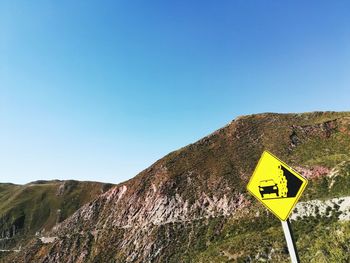 Road sign by mountain against clear blue sky