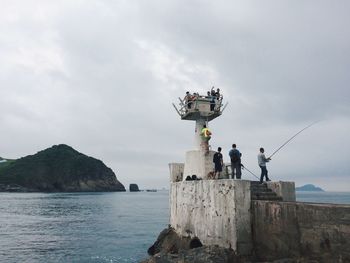 People at lighthouse by sea against sky