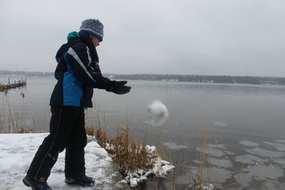 Teenage boy wearing warm clothing while standing by lake during winter