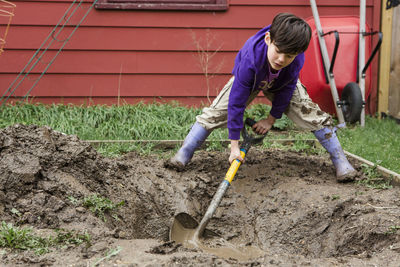 Full length of boy digging field with spade while gardening at backyard