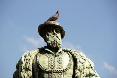 Low angle view of pigeon perching male statue against blue sky