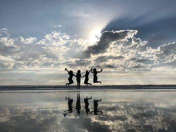 Silhouette female friends jumping over sea during sunset