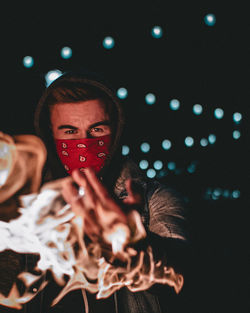 Portrait of young man wearing mask by fire in night
