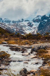 Scenic view of stream by snowcapped mountains against sky