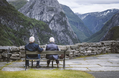 Rear view of couple sitting on bench against mountains