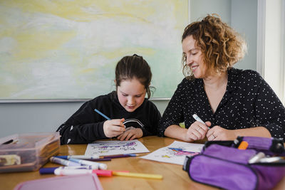 Daughter with mother coloring drawings on table at home