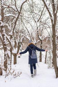 Rear view of woman wearing warm clothing with backpack walking on snow in forest
