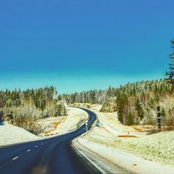 Road passing through landscape against clear blue sky