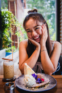 Portrait of a smiling young woman with drink sitting on table
