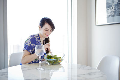 Woman eating salad while sitting by table home