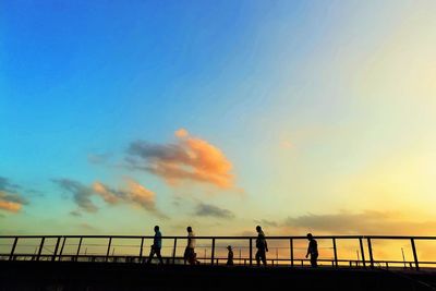People walking on footbridge against sky during sunset