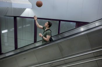 Man playing with basketball while standing on escalator