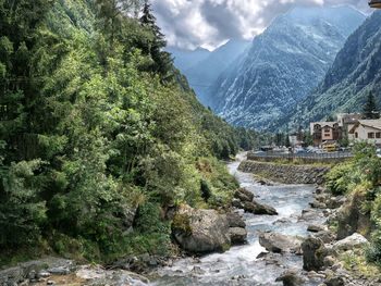 Scenic view of stream amidst trees and mountains against sky