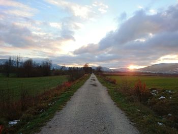 Road passing through field against cloudy sky