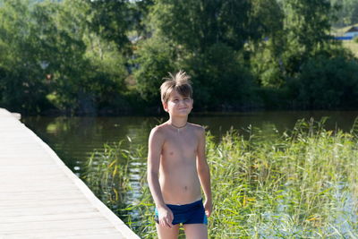 Happy boy 11 years old goes swimming on a wooden pier, on the shore of lake on a summer sunny day.