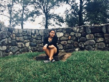 Full length of young woman sitting on stack of stone wall