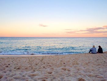 Rear view of people on beach against sky during sunset