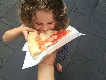 Cropped hand of parent feeding pizza slice daughter on street