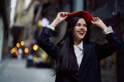 Portrait of young woman standing against city