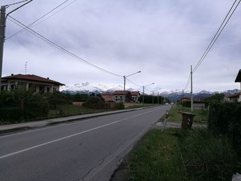 Road by electricity pylons against sky