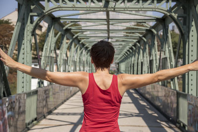 Rear view of woman with arms outstretched standing on bridge
