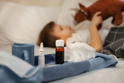 Bottle with antipyretic syrup, nasal spray and thermometer on napkin. little boy using tablet