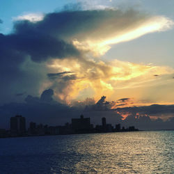 Silhouette buildings by sea against sky during sunset