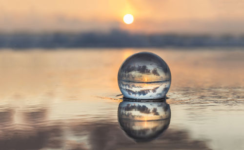 Close-up of crystal ball against sea during sunset