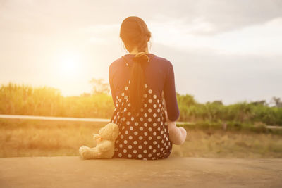 Rear view of woman standing on land against sky during sunset