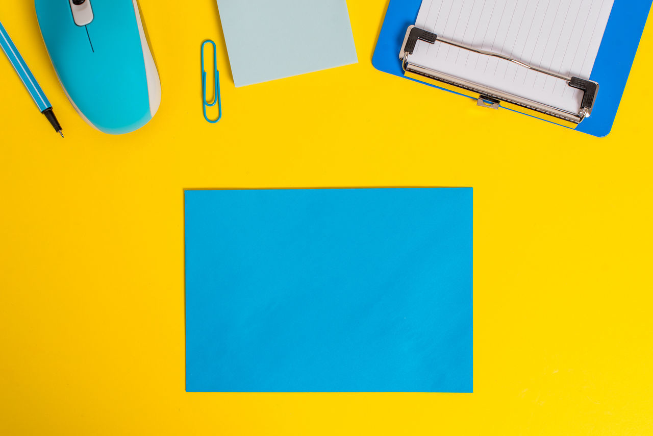 HIGH ANGLE VIEW OF YELLOW AND BLUE PAPER ON TABLE AGAINST WALL