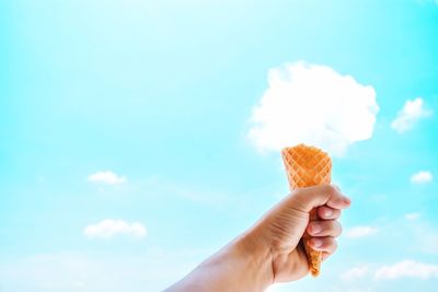 Hand holding ice cream cone against sky