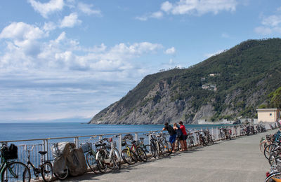 Rear view of people walking on mountain by sea against sky